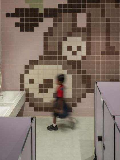 A child walks past a large sloth mural made entirely of colored tiles. We designed a different animal for each floor's washroom, creating a fun and memorable experience for the students.