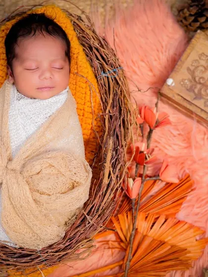 A beautifully composed overhead shot of a newborn in a nest, wrapped in a bow. The warm, earthy tones of the props create a cozy and natural feel.