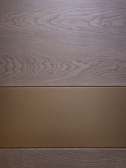 A close-up of a door combining a grey wood veneer with a smooth, matte gold metal inlay, a perfect example of mixed-material design.