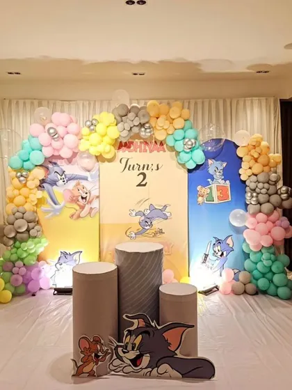 A fun-filled "Tom and Jerry" themed second birthday party. The decor includes character cut-outs, themed pedestals for the cake, and a colorful balloon arch.