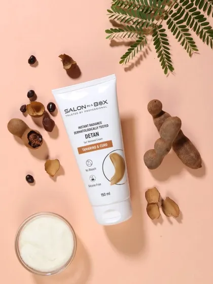 This is a top-down product photograph for a tamarind and curd-based de-tan cream. The composition includes the raw ingredients to clearly message the product's natural formulation.