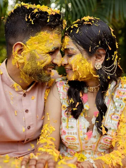 A candid, joyful moment from a Haldi ceremony, with the couple sharing a laugh, covered in turmeric and flower petals. This photo is all about capturing the raw, uninhibited fun of pre-wedding festivities.