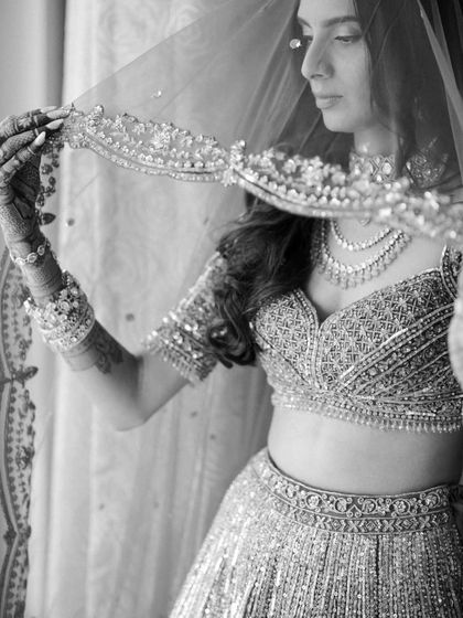 A graceful black and white bridal portrait, focusing on the bride lifting her veil, highlighting the intricate details of her outfit.