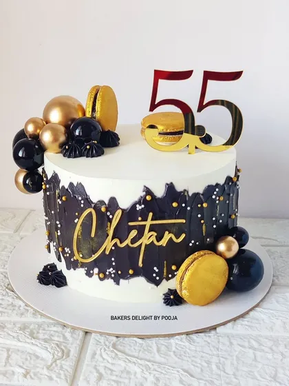 A sophisticated cake for a 55th birthday, this design features a white base with a striking black palette knife texture, accented with black and gold spheres and macarons.