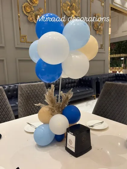Even the tables get a special touch. This is a simple yet elegant table centerpiece with blue, white, and beige balloons and a bit of dried pampas grass, matching the event's overall theme.