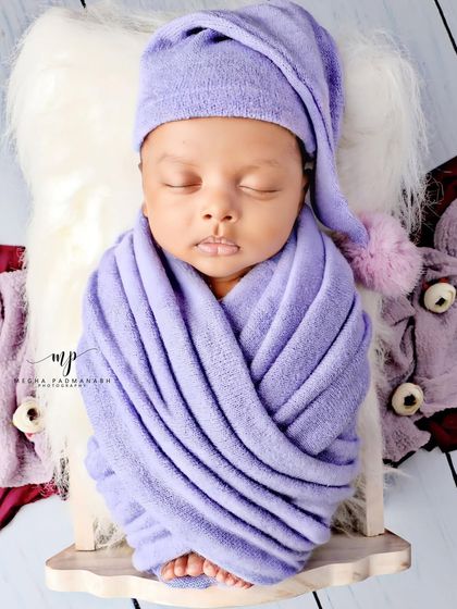 A baby boy in a purple wrap and a cute pom-pom hat, sleeping soundly.