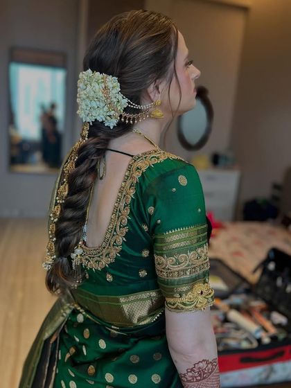 A side view of a traditional braid for a Maharashtrian bride. The hair is styled into a neat braid and decorated with fresh flowers and a side accessory, complementing her green silk saree.