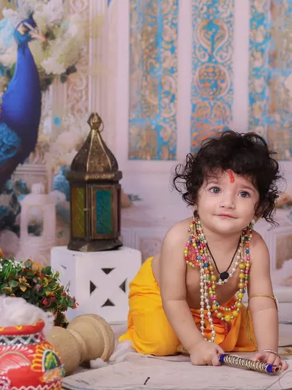 A sweet and innocent portrait of a baby dressed as Krishna, crawling on the floor amidst festive props. The soft lighting highlights his curly hair and gentle expression.