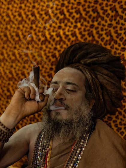 A close-up portrait of a Naga sadhu with massive dreadlocks, enjoying his chillum. The leopard print background adds to the wild and untamed aesthetic.