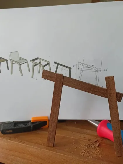 Checking the angles of the miniature chair frame against the technical drawing. This ensures the final product will have the correct posture and stability.