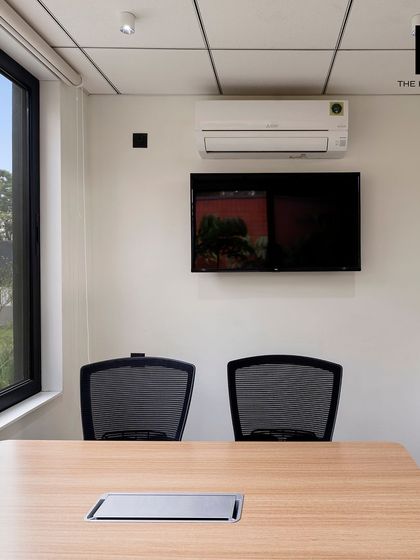 A compact meeting room or private office, fully equipped with a screen and air conditioning. The large window ensures the space feels open and connected to the exterior environment.
