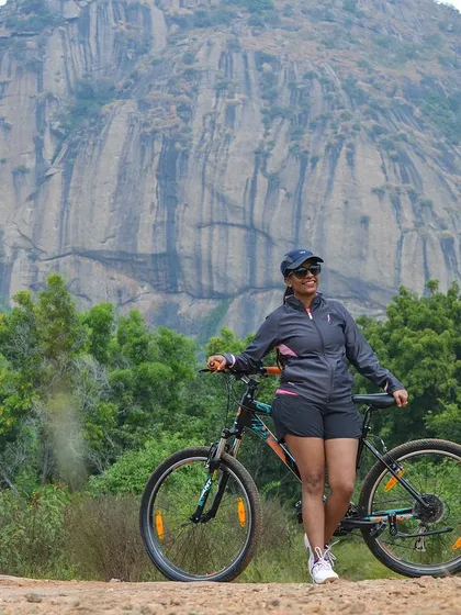 A cyclist posing with her bike against the backdrop of the iconic Ramanagara hills, famous from the movie 'Sholay'.