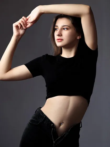 A simple and elegant portrait of a model in a black top and jeans against a grey background.