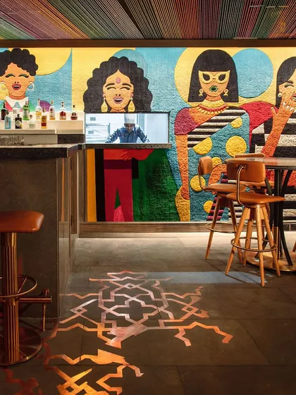 Khi Khi, a contemporary tapas bar in New Delhi, is a space defined by playful energy. The design centerpiece is a bespoke wall carpet that runs the length of the bar, its vibrant, giggling motifs creating a whimsical atmosphere that is both modern and deeply rooted in Indian artistry.