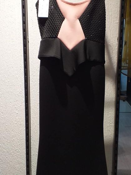 A sleek black gown with a structured peplum waist and an illusion neckline. The beaded bodice adds a touch of sparkle to this sophisticated and powerful evening dress.