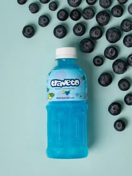 A blueberry-flavored drink surrounded by fresh blueberries in a neat flat lay. This styling clearly and beautifully communicates the product's primary flavor.