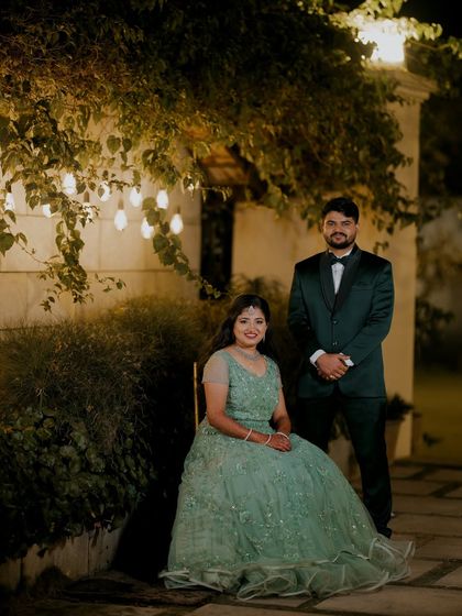 A formal portrait of the couple at their reception. The bride is seated, showcasing her gown, while the groom stands by her side, creating a timeless and elegant look.