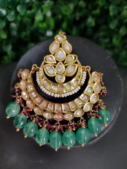 A large, crescent-shaped passa with intricate kundan work and green bead drops, perfect for a grand bridal look.