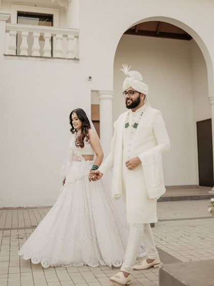 A candid walking shot capturing the couple's elegance. Dressed in white, they walk hand-in-hand, a simple and beautiful portrait of them beginning their journey together.
