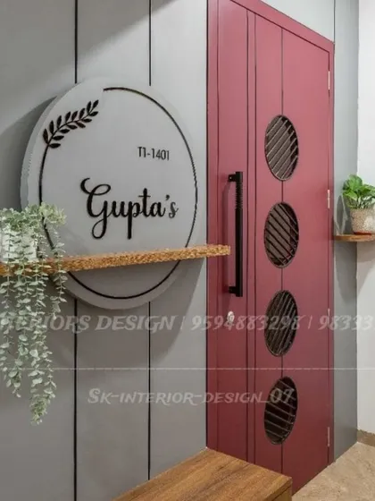 A modern and personalized entrance with a large circular nameplate and a sleek red door. The floating shelf with a trailing plant adds a touch of nature.