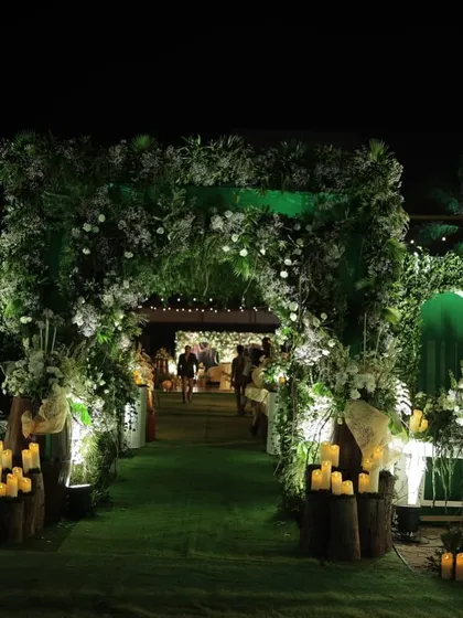 A lush green entrance I designed for an engagement party. The archway is covered in foliage and white flowers, with pillar candles on wooden stumps lighting the path and creating a warm, welcoming ambiance.
