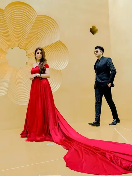 This shot captures a dynamic, fashion-inspired moment during a pre-wedding shoot. The contrast between the bride's flowing red gown and the groom's sharp black suit creates a visually striking image.