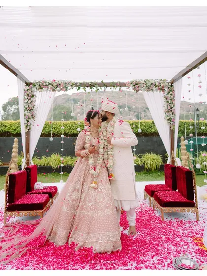 A wide shot of the couple sharing a kiss under their beautiful mandap, covered in flowers.