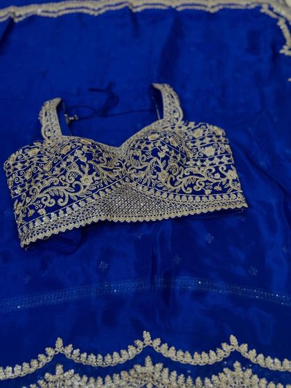 A detailed view of a party-ready ensemble. This royal blue blouse and saree set is made from Chinon fabric and features heavy silver-toned embroidery with a scalloped border, perfect for making a statement at any celebration.