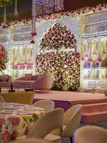 A side view of the grand engagement stage, showing the depth of the floral arch and the elegant pink seating. The floral-printed tablecloth in the foreground ties the whole look together.