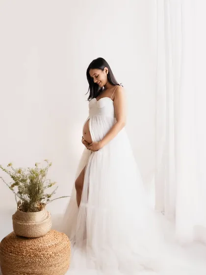So angelic and serene. This mom-to-be chose a simple, elegant white tulle gown from my collection for her studio session. The soft lighting from the window creates a gentle glow, perfect for a peaceful solo maternity portrait.