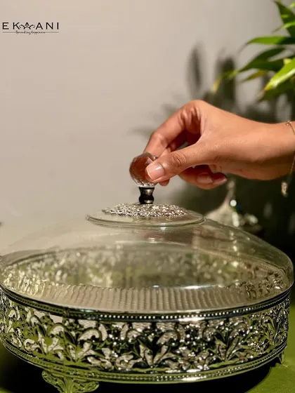 An intricately designed round serving box, perfect for storing dry fruits or delicacies in style. The detailed silver filigree work adds a regal touch to your table.