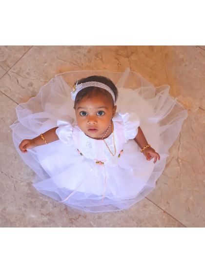 A beautiful bird's-eye view of a baby girl in a white dress, looking like a little angel. The simple, clean flooring helps to emphasize the texture and shape of her outfit.
