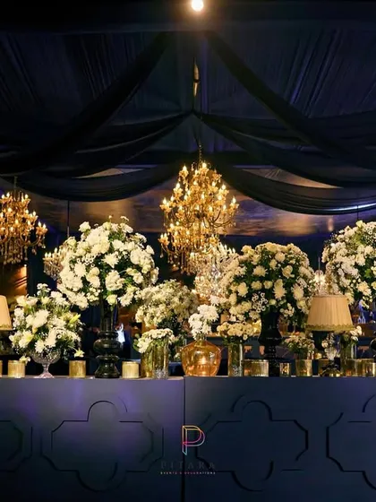 The bar was a focal point, featuring a mirrored front with a quatrefoil pattern and a backdrop of deep blue. It was topped with massive urns of white florals and golden lamps, reflecting the grandeur of the evening.