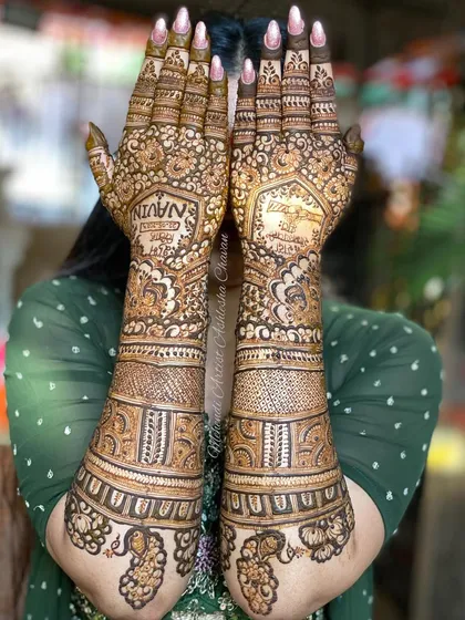 The back of a bridal mehendi, personalized with the groom's name. This view shows the full arm coverage and the detailed patterns that wrap around the hands.