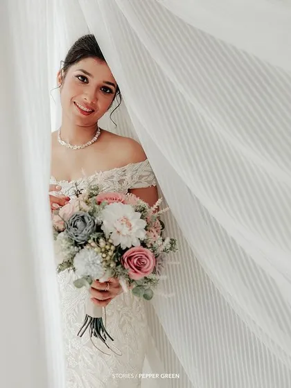 A dreamy portrait of the bride peeking through a sheer white curtain, her smile soft and inviting.