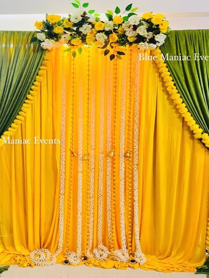 A classic Haldi or Mehendi backdrop with green and yellow drapes and hanging strings of marigolds and white tuberoses.