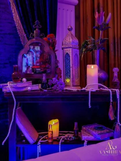 A side table vignette in the Genie lounge, styled with an ornate mirror, a lantern, scattered books, and pearl strings to create a magical, lived-in feel.