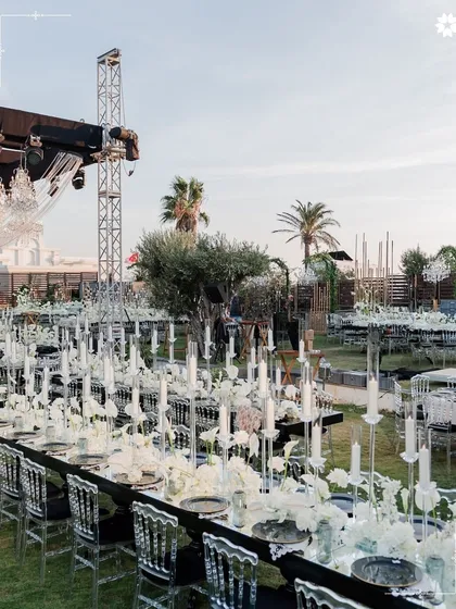 An elaborate outdoor reception setup where long tables, crystal clear chairs, and countless candles create a landscape of modern luxury. We specialise in executing large scale events with precision and a flair for the dramatic.