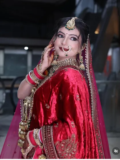 A smiling bride in her red velvet lehenga, showcasing her nose ring and heavy bridal jewellery. The look is both traditional and joyful.