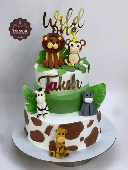 A "Wild One" animal theme cake for a first birthday. This two-tier cake features cute, hand-crafted fondant animals like a lion, monkey, and giraffe, with two different flavours inside.