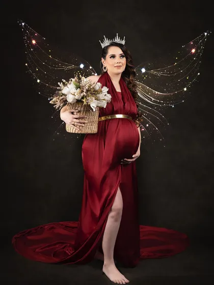 A magical portrait where the client becomes a fairy queen. Wearing a crown and a red satin gown, she is adorned with sparkling fairy wings for a truly enchanting photo.