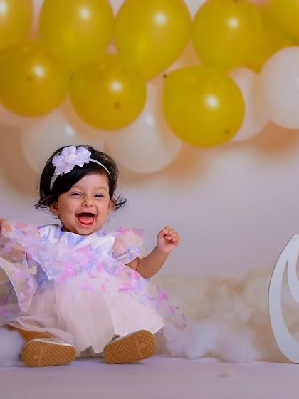 Pure happiness. This little princess is all giggles during her first birthday photoshoot, surrounded by clouds of fluff and balloons.