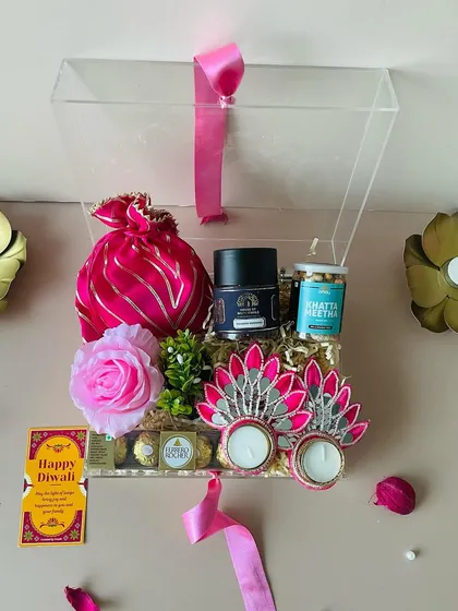 The clear acrylic box beautifully showcases the premium goodies inside. The pink ribbon adds a soft, celebratory touch to this elegant hamper.