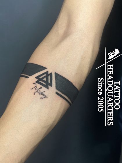A modern armband design that combines solid black bands with a Valknut symbol and the name "Mickey" in fine script.