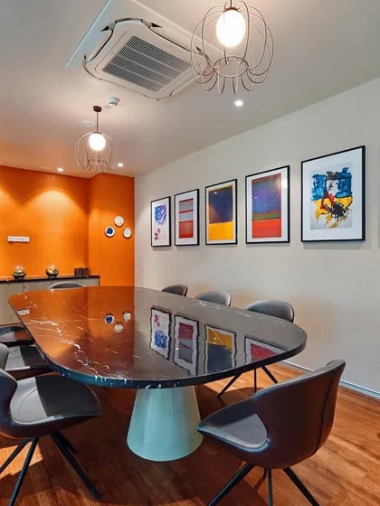 A vibrant meeting room with a bold orange accent wall and a gallery of colorful abstract art. The black marble table adds a touch of elegance to the otherwise playful space.