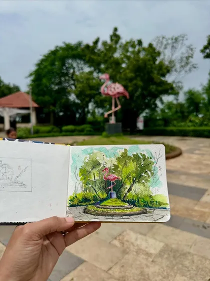 My finished watercolour sketch of the flamingo statue, held up against the real thing. I used loose, expressive strokes to capture the surrounding greenery.