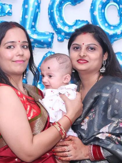 A duplicate of the previous image, showing two women with a newborn at a celebration, highlighting our event coverage for new arrivals.