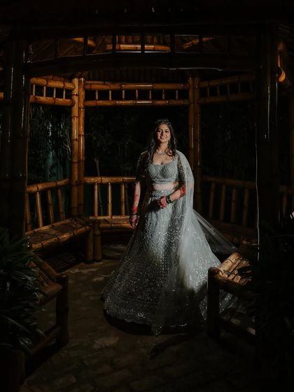 A stunning portrait of the bride in a bamboo gazebo. The dramatic lighting highlights the sparkle of her lehenga and the beautiful finish of her makeup.