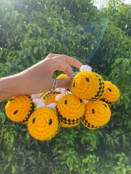 Holding up a handful of my cheerful bee keychains against a beautiful green backdrop. These are perfect for adding a touch of nature to your product offerings.