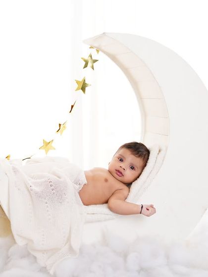 A dreamy baby portrait with a little one resting on a crescent moon prop, surrounded by soft clouds and golden stars.